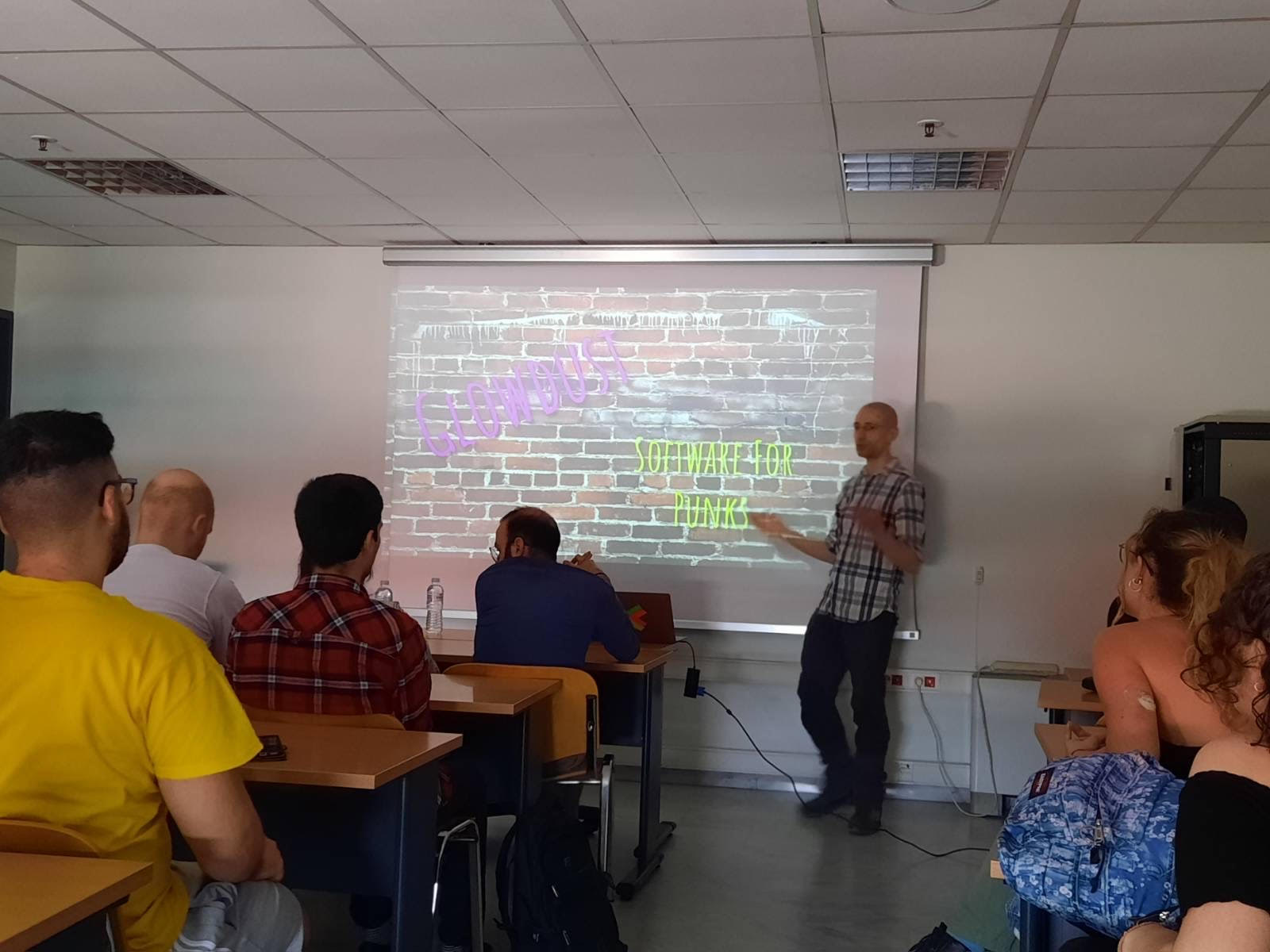 The author standing in front of a classroom with students. Behind him a projected slide of a brick wall with the text Glowdust software for punks written over it, in bright colored letters
